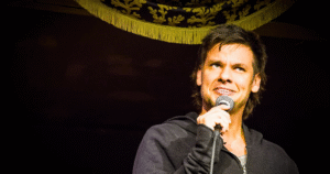 1. A Man Stands With A Microphone In Front Of A Stage Curtain, Ready To Speak Or Perform.